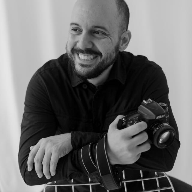 Elkin Carvajal sonriendo con una cámara en la mano, en blanco y negro