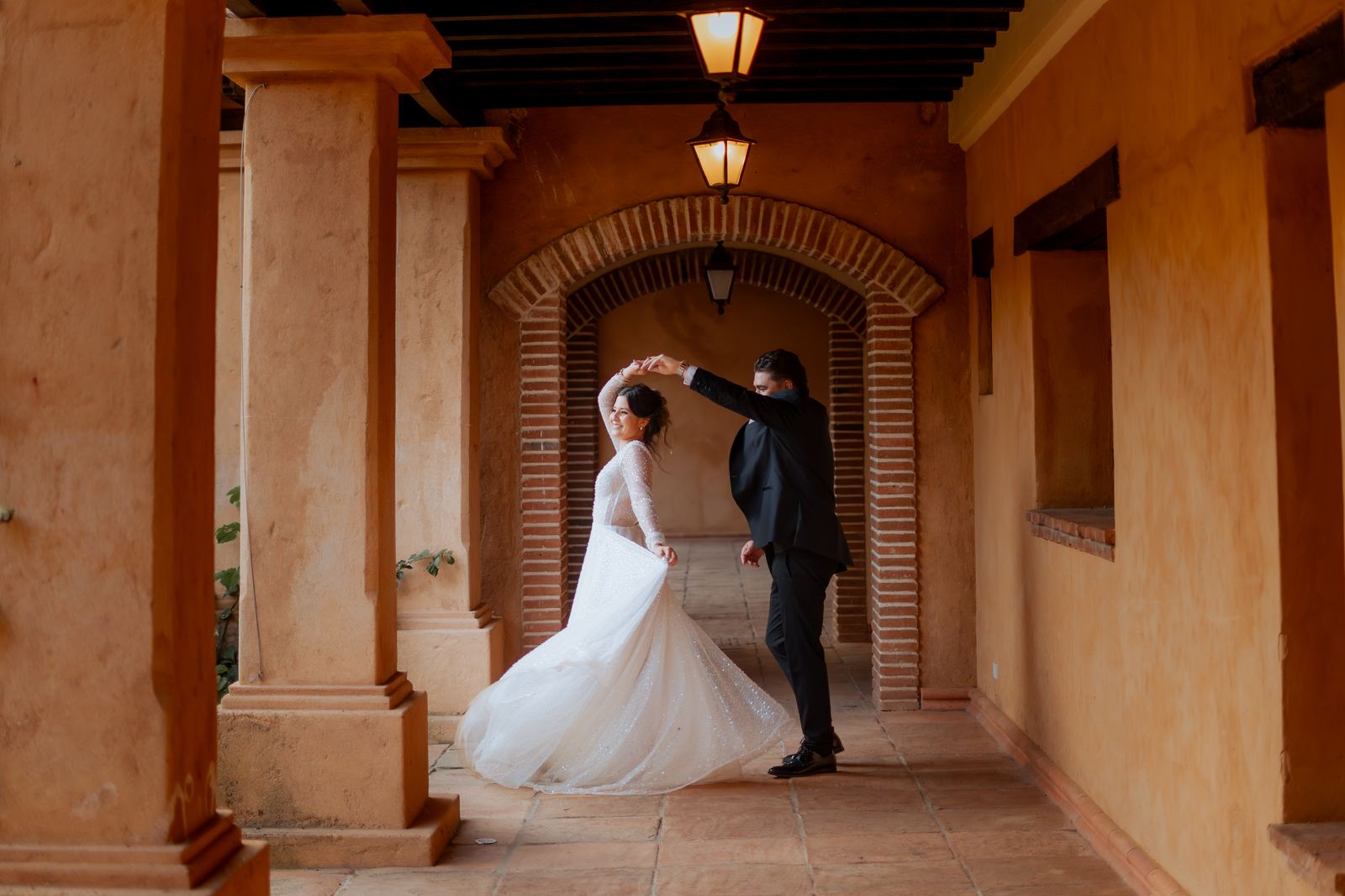 Los novios bailando en un corredor de ladrillo con farolas